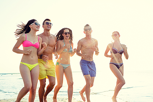 friendship, sea, summer vacation, holidays and people concept - group of smiling friends wearing swimwear and sunglasses running on beach