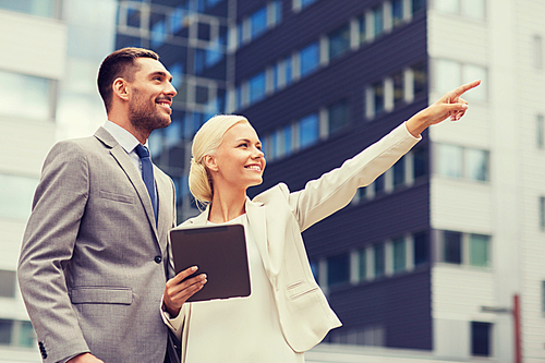 business, partnership, technology and people concept - smiling businessman and businesswoman with tablet pc computer over office building