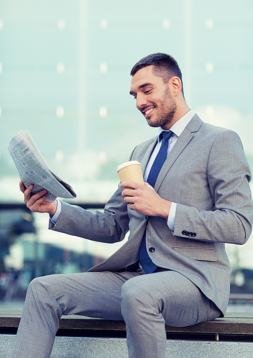 business, hot drinks and people and concept - young smiling businessman with paper coffee cup and newspaper over office building