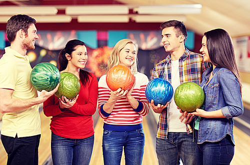 people, leisure, sport, friendship and entertainment concept - happy friends holding balls and talking in bowling club