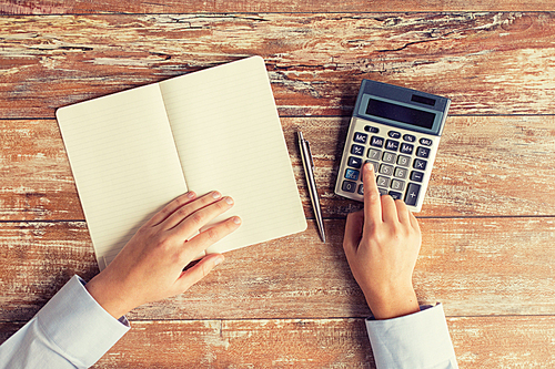 business, education, people and technology concept - close up of female hands with calculator, pen and notebook on table