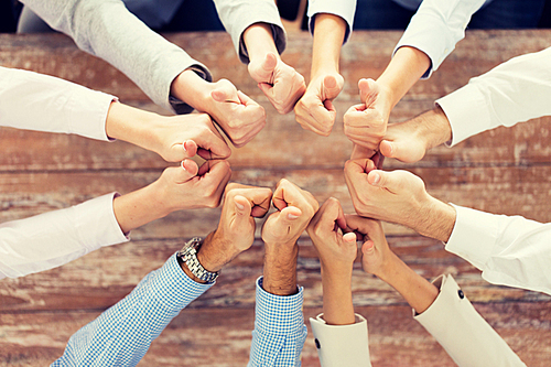 business, people, gesture and team work concept - close up of creative team showing thumbs up and sitting at table in office