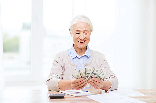 business, savings, annuity insurance, age and people concept - happy senior woman with calculator and bills counting dollar money at home