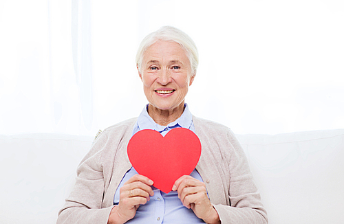 age, holidays, valentines day, love and people concept - happy smiling senior woman with red heart shape at home