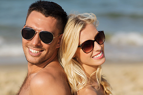 love, travel, tourism, summer and people concept - smiling couple on vacation in swimwear sitting on beach back to back