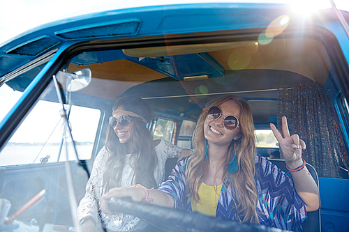 summer holidays, road trip, vacation, travel and people concept - smiling young hippie women driving minivan car and showing peace gesture