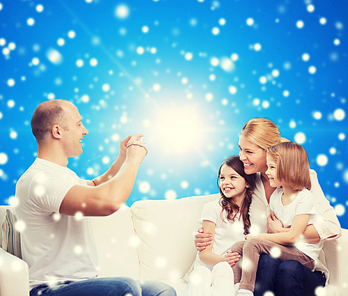 family, holidays, christmas technology and people - smiling mother, father and little girls with camera over blue snowy background