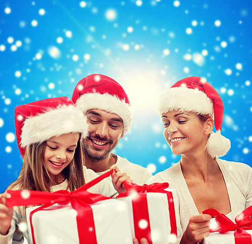 family, christmas, generation, holidays and people concept - happy family in santa helper hats with gift boxes sitting over blue snowy background