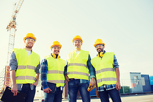 business, building, teamwork, technology and people concept - group of smiling builders in hardhats with tablet pc computer and clipboard outdoors