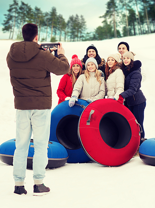 winter, leisure, sport, friendship and people concept - group of smiling friends with snow tubes taking picture by tablet pc computer outdoors