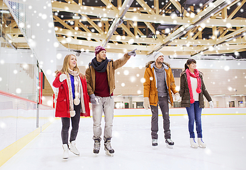 people, friendship, sport, gesture and leisure concept - happy friends pointing finger on skating rink