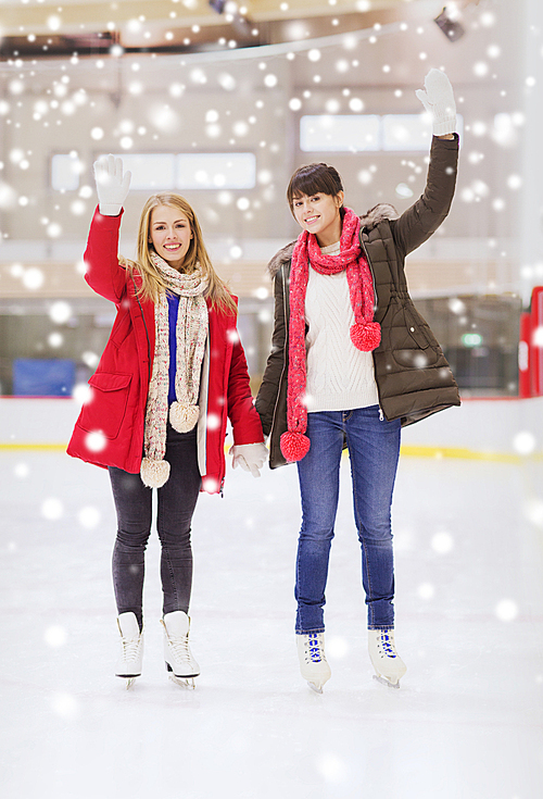 people, women, friendship, sport and leisure concept - two happy girls friends waving hands on skating rink