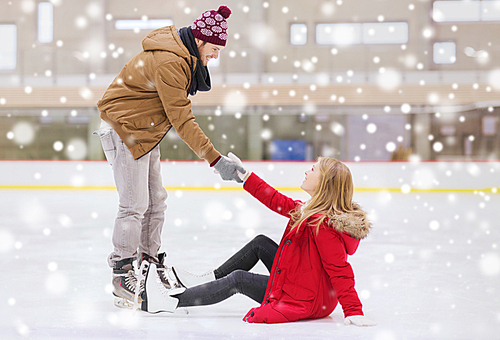 people, friendship, sport and leisure concept - smiling man helping women to rise up on skating rink