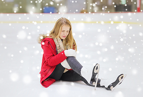 people, sport, trauma, pain and leisure concept - young woman fell down on skating rink and holding to her knee