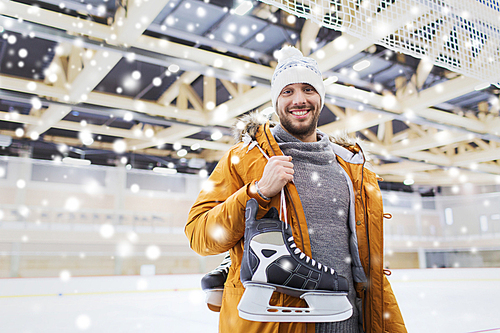 people, sport and leisure concept - happy young man with ice-skates on skating rink