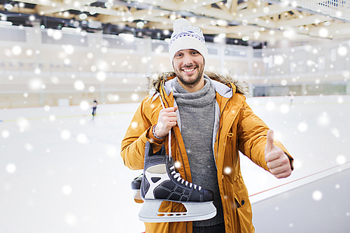 people, sport, gesture and leisure concept - happy young man with ice-skates showing thumbs up on skating rink