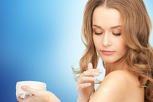 beauty, people and health concept - beautiful smiling woman cleaning face skin with cotton pad over blue background