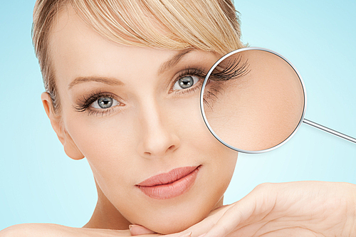 beauty, people, lash extension and makeover concept - beautiful young woman face over blue background with lashes in magnifying glass