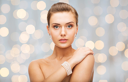 beauty, luxury, people, holidays and jewelry concept - beautiful woman with pearl earrings and bracelet over lights background