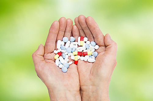 age, medicine, health care and people concept - close up of senior woman cupped hands with pills over green natural background