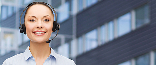 business, people, technology and communication concept - happy asian female helpline operator in headset over city office building background