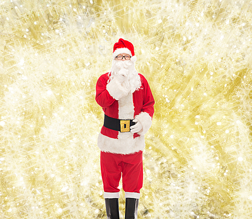 christmas, holidays and people concept - man in costume of santa claus making hush gesture over yellow lights background