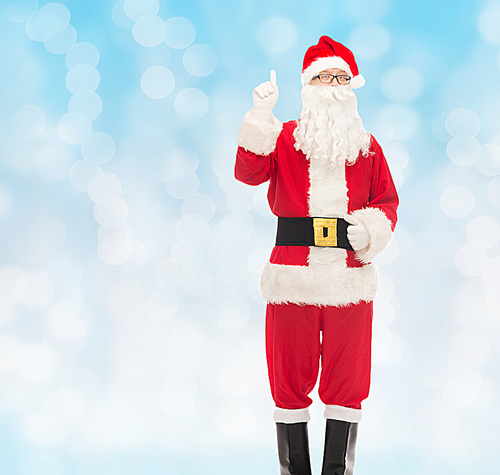 christmas, holidays, gesture and people concept - man in costume of santa claus pointing finger up over blue lights background