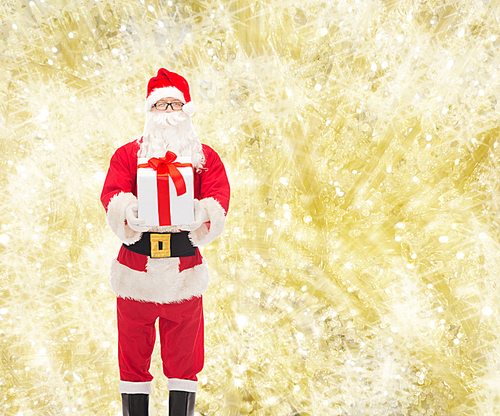 christmas, holidays and people concept - man in costume of santa claus with gift box over yellow lights background