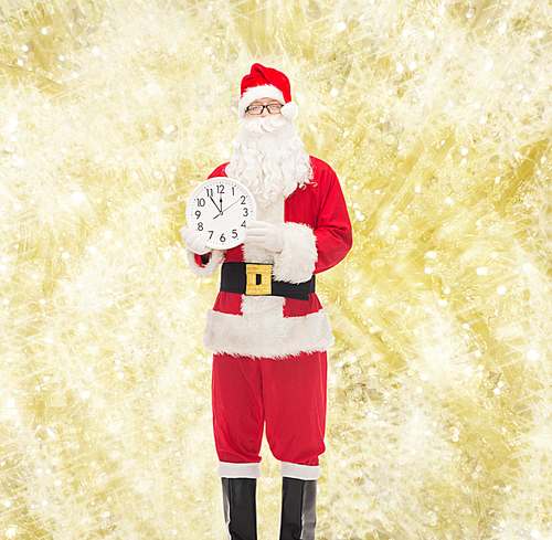 christmas, holidays and people concept - man in costume of santa claus with clock showing twelve over yellow lights background