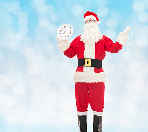 christmas, holidays and people concept - man in costume of santa claus with clock showing twelve over blue lights background