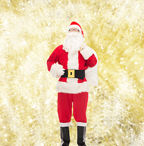 christmas, holidays and people concept - man in costume of santa claus with bag over yellow lights background