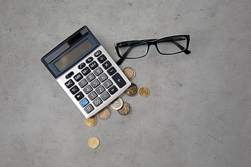 busines, finance, money and bookkeeping concept - calculator, eyeglasses and euro coins over gray concrete background