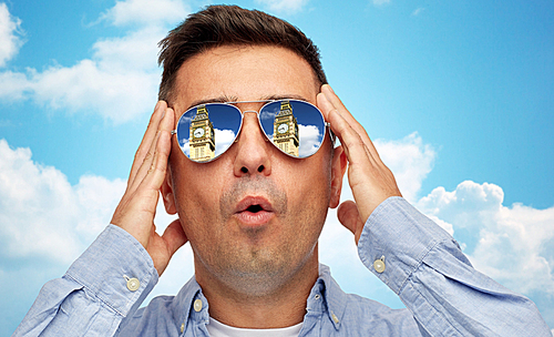 travel, tourism, sightseeing, emotions and people concept - face of man in sunglasses looking at big ben tower over blue sky and clouds background