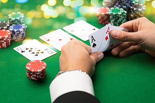 casino, gambling, poker, people and entertainment concept - close up of poker player with playing cards and chips at green casino table over holidays lights background