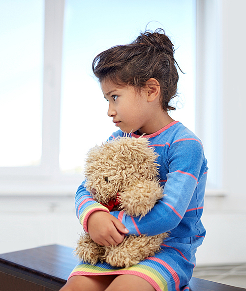 childhood, sadness, loneliness and people concept - sad little girl with teddy bear toy at home
