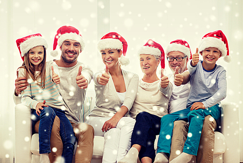 family, happiness, generation, holidays and people concept - happy family in santa helper hats sitting on couch and showing thumbs up gesture at home