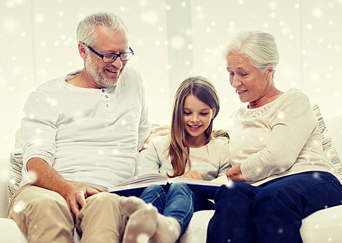 family, generation, education and people concept - smiling grandfather, granddaughter and grandmother with book or photo album sitting on couch at home