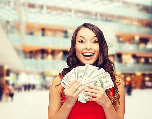 holidays, banking, winning and people concept - smiling woman in red dress with us dollar money over shopping centre background