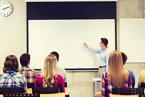 education, high school, teamwork and people concept - smiling teacher standing in front of students and writing something on white board in classroom