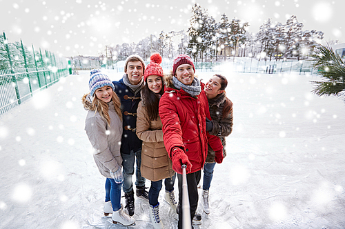 people, friendship, technology and leisure concept - happy friends taking picture with smartphone selfie stick on ice skating rink outdoors