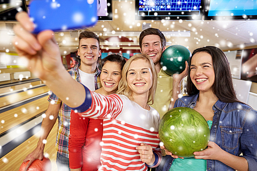 people, leisure, sport, friendship and entertainment concept - happy friends taking selfie with smartphone in bowling club at winter season