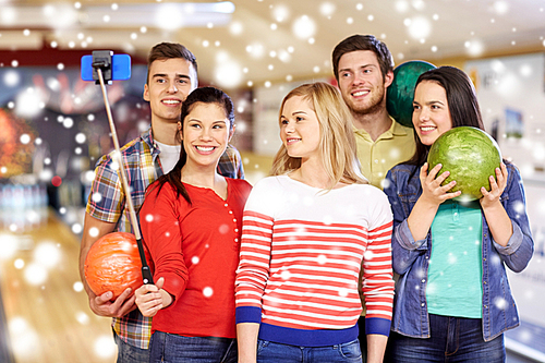 people, leisure, sport, friendship and entertainment concept - happy friends taking selfie with smartphone on monopod in bowling club at winter season