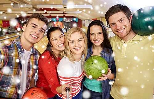 people, leisure, sport, friendship and entertainment concept - happy friends taking selfie with smartphone on monopod in bowling club at winter season