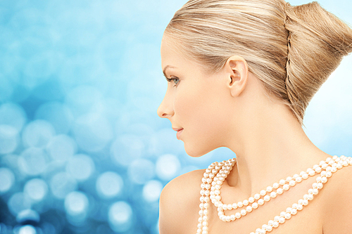 beauty, luxury, people, holidays and jewelry concept - beautiful woman with sea pearl necklace or beads over blue lights background