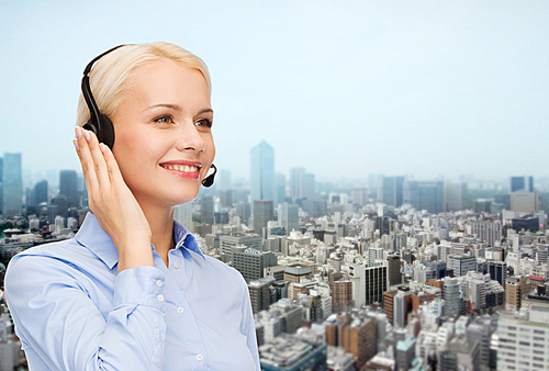 business, people, technology and communication concept - happy female helpline operator in headset over city background