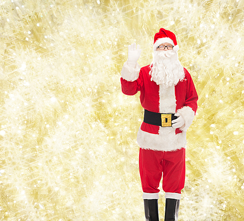 christmas, holidays, gesture and people concept - man in costume of santa claus waving hand over yellow lights background