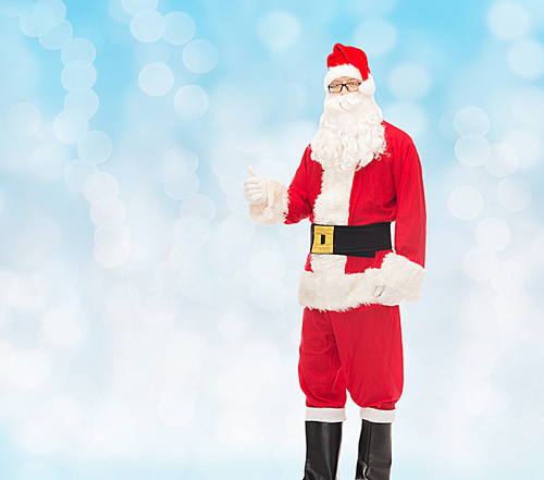 christmas, holidays, gesture and people concept- man in costume of santa claus showing thumbs up over blue lights background