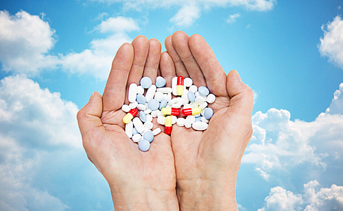 age, medicine, health care and people concept - close up of senior woman cupped hands with pills over blue sky and clouds background
