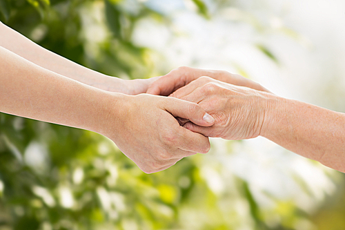 people, age, family, care and support concept - close up of senior woman and young woman holding hands over green natural background