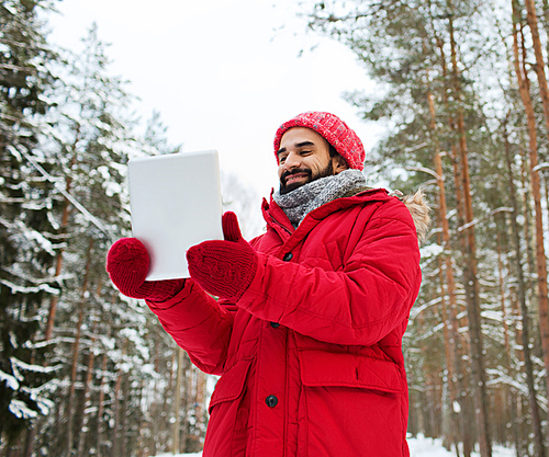 christmas, season, technology and people concept - happy man with tablet pc computer in winter forest